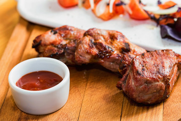 Close up roasted pork neck with spices, vegetables and ketchup on wooden board