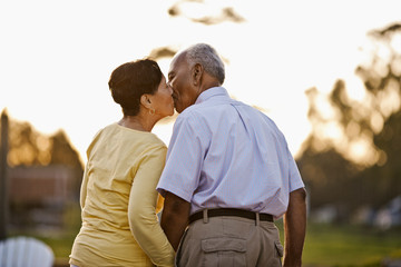 Happy senior couple kissing while standing together in the back yard.