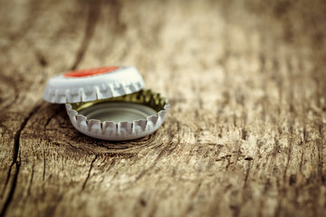 bottle cap from a beer bottle on wooden background. several beer lids lie in pile, behind them bottle. close up. soft selective focus.