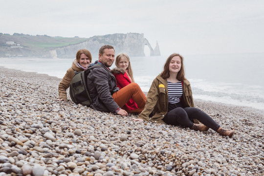Dad with mom and two daughters sitting on the beach of  Etretat