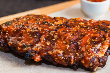 Close up roasted pork ribs with spices, jalapeno and ketchup on wooden board