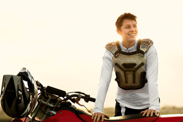 Smiling young female motocross rider leaning on her dirt bike at the track.