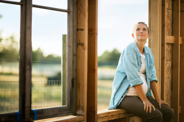 Expectant mother sitting in the window frame of a home under construction.