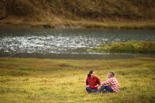 Mature couple sitting in a lakeside field.