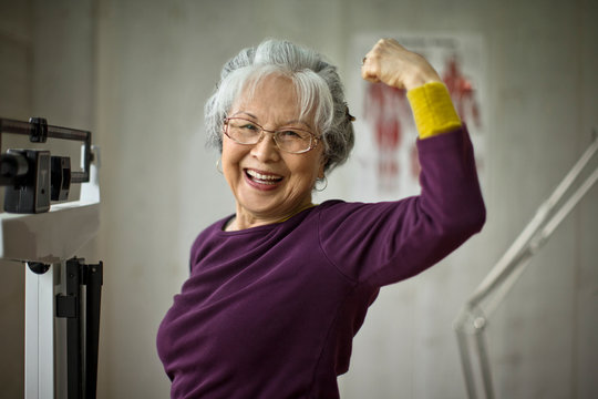 Smiling senior woman flexing her muscles while standing on scales.