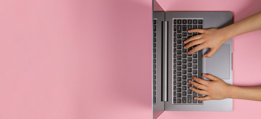 Fototapeta na wymiar Kid hands typing on laptop computer keyboard, top view, pink banner background