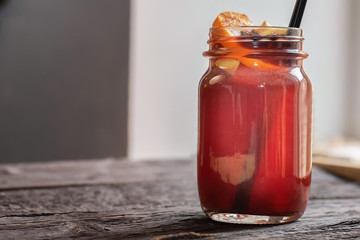 Close up glass jar with hot mulled wine and straw on dark wooden table