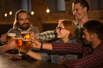 Friends hanging out and resting in beer pub or bar. Positivity company clinking their glasses and pints of beer. Hands holding glasses full of delicious lager.