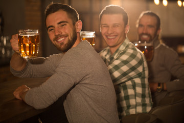 Handsome and positive men showing beer glasses they holding in hands. Male clients looking at camera, posing and smiling. Three cheerful men enjoying weekend in beer pub.