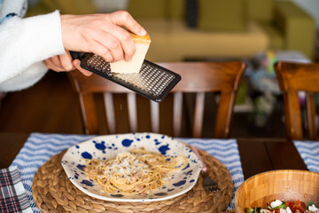 woman hands grating parmesan cheese on pasta carbonara