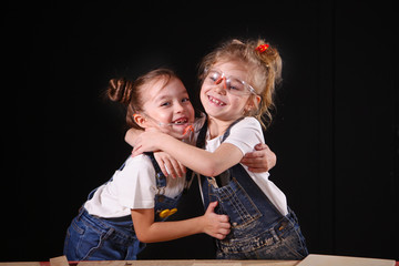 Two little girls, dressed in overalls, hugging in the carpenter's shop after class. The concept of teaching applied arts.