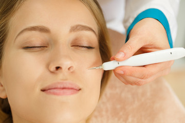 Closeup of face of female client during procedure of blackheads removing in beauty salon. Professional cosmetologist keeping in hand tool for face cleaning. Concept of cleansing and skin care.
