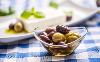 Green and red olives in bowl with olive oil and greek feta cheese in the background
