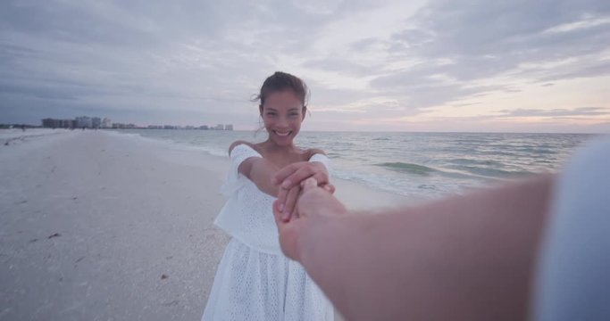 POV romantic Young couple holding hands woman leading boyfriend at beach sunset. Travel holidays vacation concept.