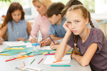 Fototapeta premium Girl sitting at table, leaning on arm, tired and bored.