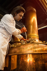 Serious brewer concentrated on process of brewing. Worker in uniform holding steel ladle above opened bronzed brew kettle. Professional specialist working in beer industry.