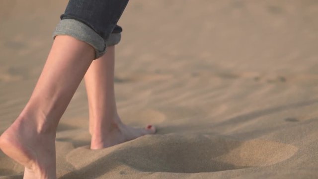 Close up, Slow motion. Woman feets walking on golden sand at the beach .