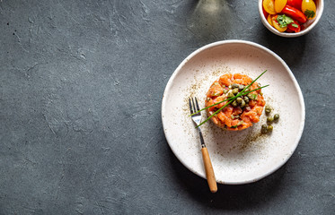 SALMON TARTAR with capers and purple onion on white plate, gray background