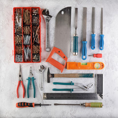 Set of construction tools for home on a white cement background. Level, saw, glasses, angle measure, wrench, spanner, paint roll, hammer, cutter, pliers, screws and more.