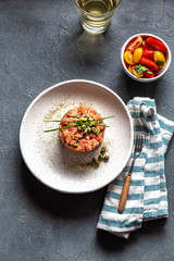 SALMON TARTAR with capers and purple onion on white plate, gray background