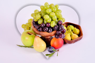 Light and dark grapes in a wooden bowl with an apple pear plum and figs on a white background.Fruit still life