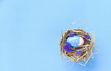 Easter eggs in basket nest decoration with purple statice flowers on blue background