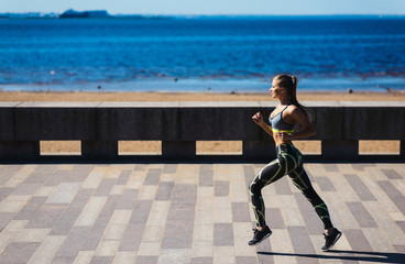Young sexy girl model runs in the city on the embankment in the morning. Workout fitness healthy...