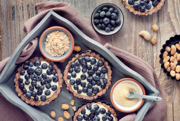 Top view on wholegrain blueberry tarts with vanilla cream on rustic wood