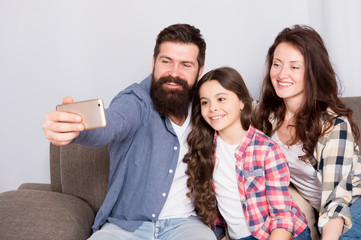 Obraz premium Family spend weekend together. Use smartphone for selfie. Friendly family having fun together. Mom dad and daughter relaxing on couch. Family posing for photo. Capture happy moments. Family selfie