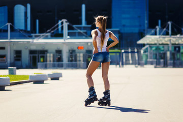 Portrait of a beautiful sexy young blonde girl on roller skates, in denim shorts and a T-shirt. Smiling and lookind at camera. Hot summer day. Outdoor city sports. Healthy lifestyle concept