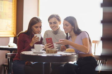 Three girlfriends looking at smartphone screen, spending time together in cafe.