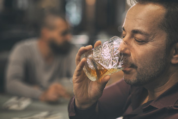 Side view of handsome man drinking delicious whiskey. Bearded man holding crystal glass of scotch and smelling it with closed eyes. Client of bar tasting elite alcohol.