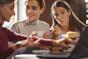 Three friends drinking coffee and eating cake during lunch break.