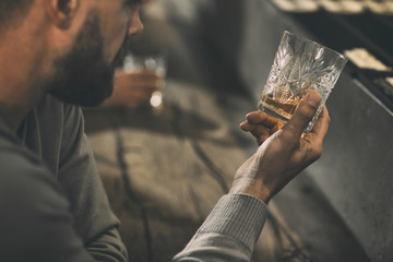 Close up of man's hand holding crystal glass of whiskey or brandy. Bearded man drinking and tasting...