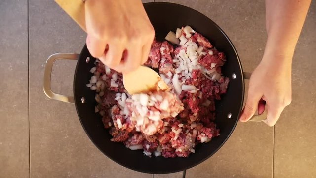Overhead timelapse, person mixes onion and garlic into pan of meat