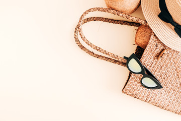 Summer concept. Straw bag, glasses, hat, coconut on pastel beige background. Flat lay, top view, copy space