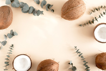 Summer composition. Frame made of coconut, eucalyptus branches on pastel beige background. Flat lay, top view, copy space