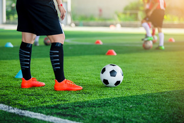 coach of soccer player standing and  stepping on the ball with blurry of young boy soccer player training.