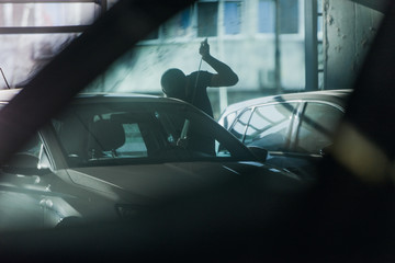 Thief robbing a car on parking lot, shot through another car