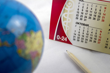a globe and a calendar with a pen on a white background. Focus on the calendar