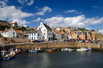 Boats moored at stone pier in Crail Harbour with Crail House lookout turret over the North Sea in...