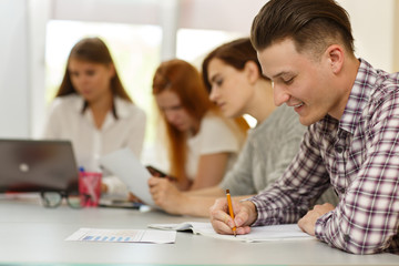 Side view of happy student writing in notes and doing test during lesson in modern school. Young...