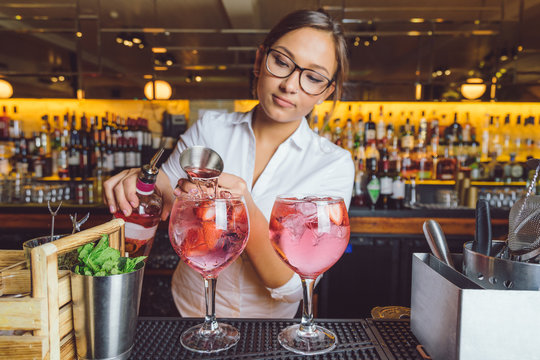 female beautiful smart bartender mixologist bar person makes prepares gin tonic cocktail drink pink mint fish bowl glass