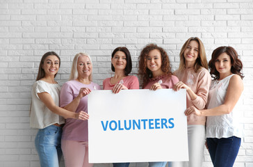 Women wearing silk ribbons holding poster with space for text against brick wall. Breast cancer awareness concept