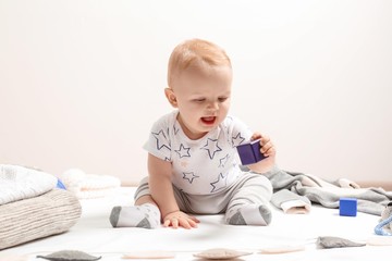 Little boy in cute clothes sitting on floor against light background. Baby accessories