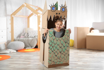 Cute little girl in cardboard costume of dinosaur at home