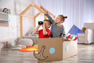 Cute little kids playing with binoculars and cardboard boat in bedroom