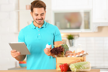 Young man with tablet PC and products in kitchen. Food delivery service