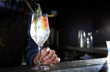 Barman making grapefruit gin tonic cocktail at counter in pub, closeup. Space for text