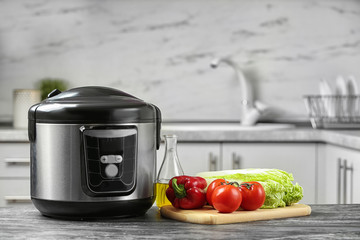Modern multi cooker and products on table in kitchen. Space for text